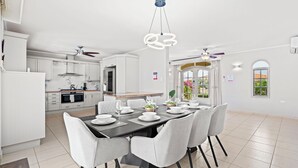 Una cucina moderna con mobili bianchi, un'area pranzo con tavolo nero e sedie grigie e una ventola a soffitto.