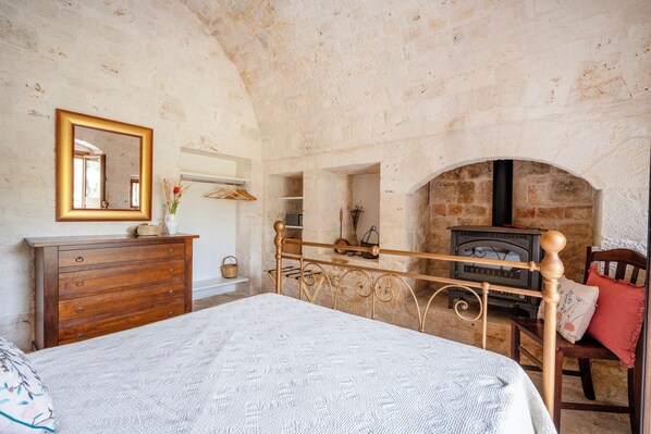 Quarto com cama de madeira, penteadeira, espelho e lareira de pedra.