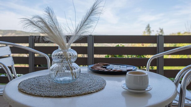 A round table with a woven placemat, a clear glass vase with white feathers, a plate of cookies, and a cup of coffee.