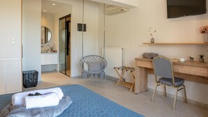 A modern bedroom with a bed, a desk, a chair, a TV, and a bathroom visible through an open door.