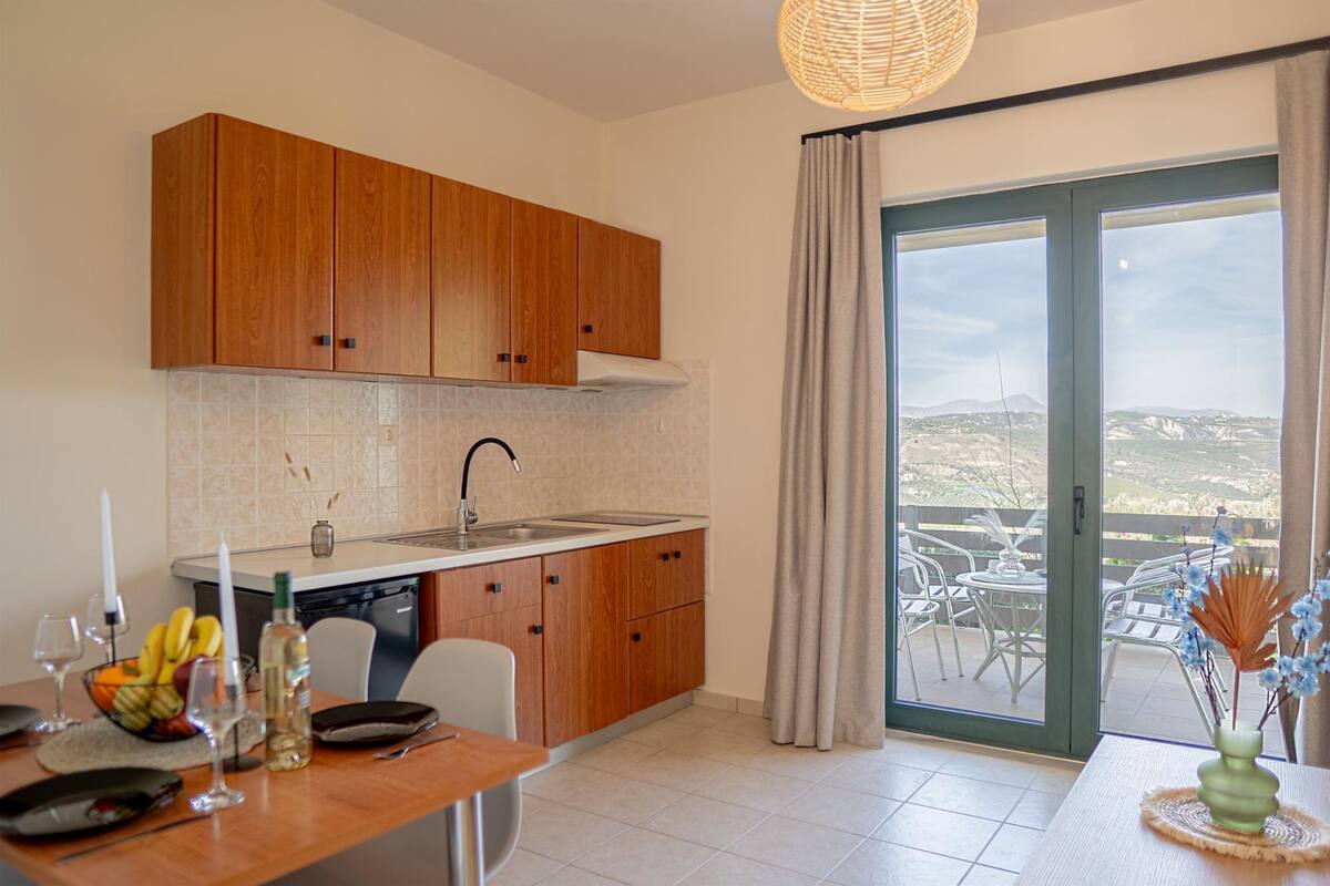 Una cocina moderna con armarios de madera, una mesa de comedor y vistas a un balcón con mobiliario exterior.