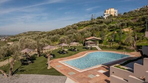 A swimming pool with a tiled deck, lounge chairs, umbrellas, and a gazebo.