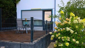 A fenced outdoor area with a table and chairs, a building with a garage door, and a flowering plant.