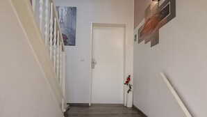 A hallway with a wooden floor, a white door, and a small potted plant with red flowers.