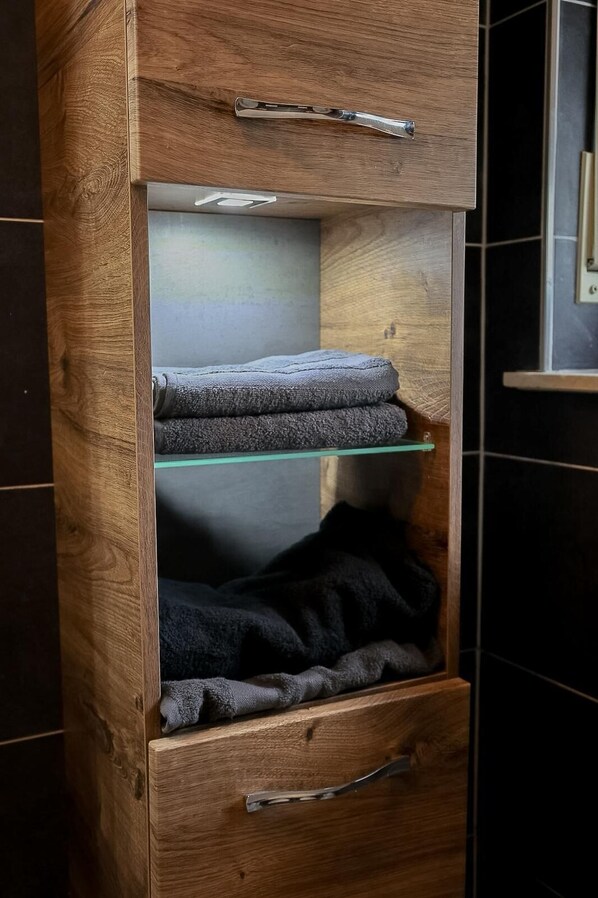 A wooden cabinet with a glass shelf holding folded towels and a drawer below. - Bibo City Apartment 2 with terrace (Bielefeld)