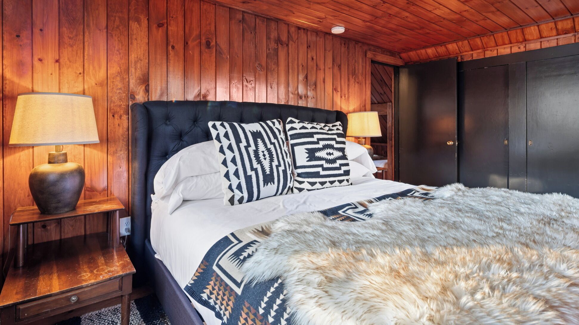 A wooden-paneled bedroom with a large bed, two bedside lamps, and a fur throw. - NEW LISTING!! Charming home in STOWE VILLAGE steps to Trails, Dining & Adventure (Stowe)