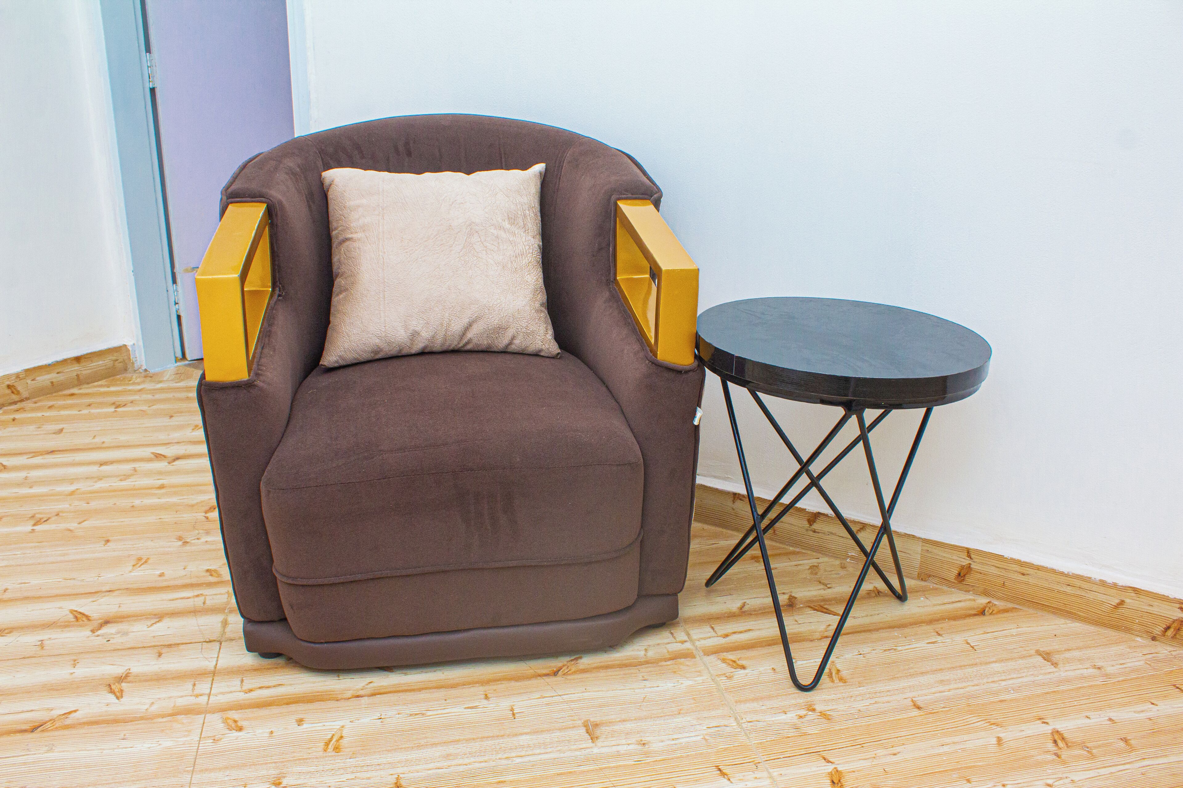 A brown armchair with a beige cushion and a small round table with a black top and metal legs.