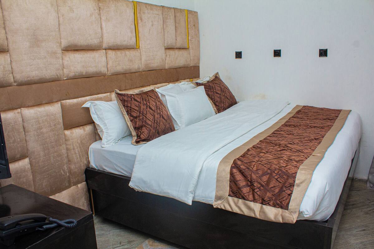Habitación de hotel con una cama grande, un cabecero y una mesita de noche con teléfono.