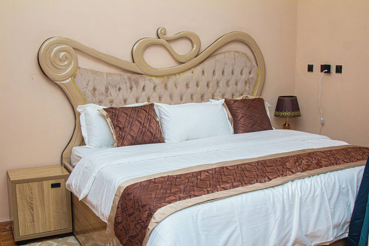 Una cama bien hecha con una colcha estampada, una mesita de noche de madera y una lámpara de pared.