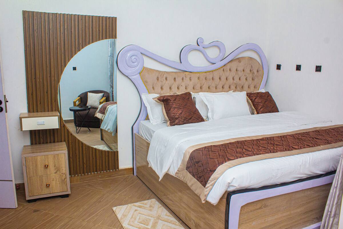 Un dormitorio con una cama, una mesita de noche de madera, un espejo y una pequeña mesa.