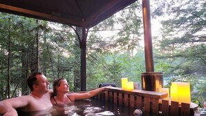 A wooden hot tub with a wooden bench and candles, surrounded by trees.