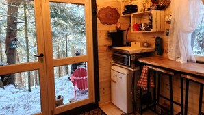 A cozy cabin kitchen with a wooden interior, a built-in oven, and a window overlooking a snowy forest.