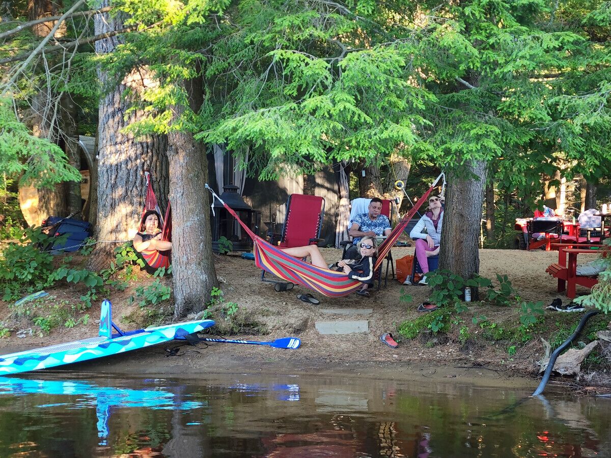 Un terrain de camping situé au bord d’une rivière, équipé de hamacs, d’un canoë et de tables de pique-nique.