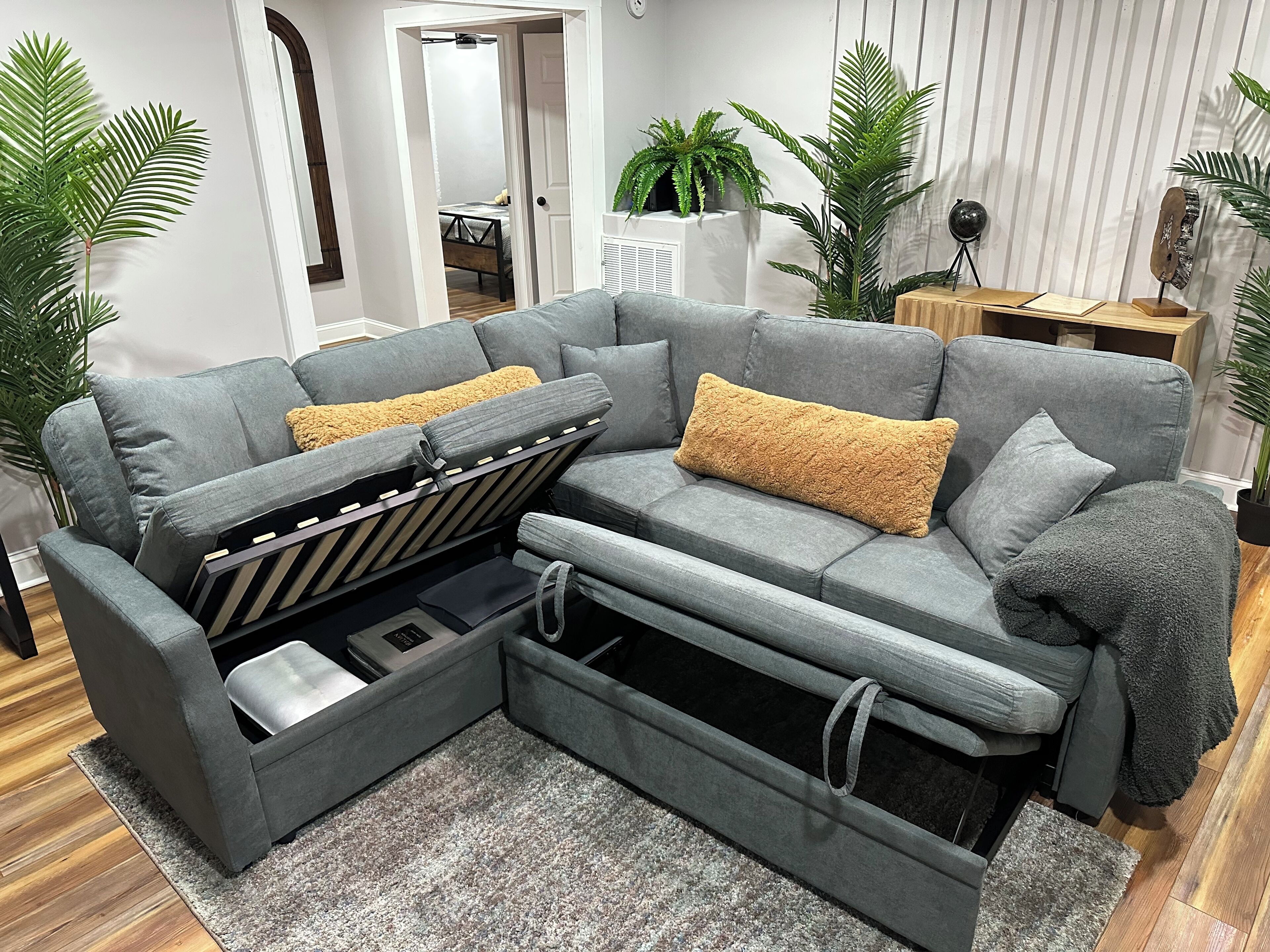 Ein graues Ecksofa mit Stauraum, zwei gelbe Zierkissen und eine graue Decke.