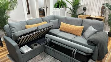 Ein graues Ecksofa mit Stauraum, zwei gelbe Zierkissen und eine graue Decke.