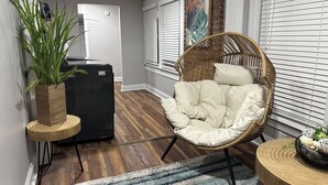 A living room with a wicker chair, a potted plant, a black refrigerator, and a blue striped rug. - Winston Salem 3Bd 2Ba GAME ROOM mins to Downtown (Winston-Salem)