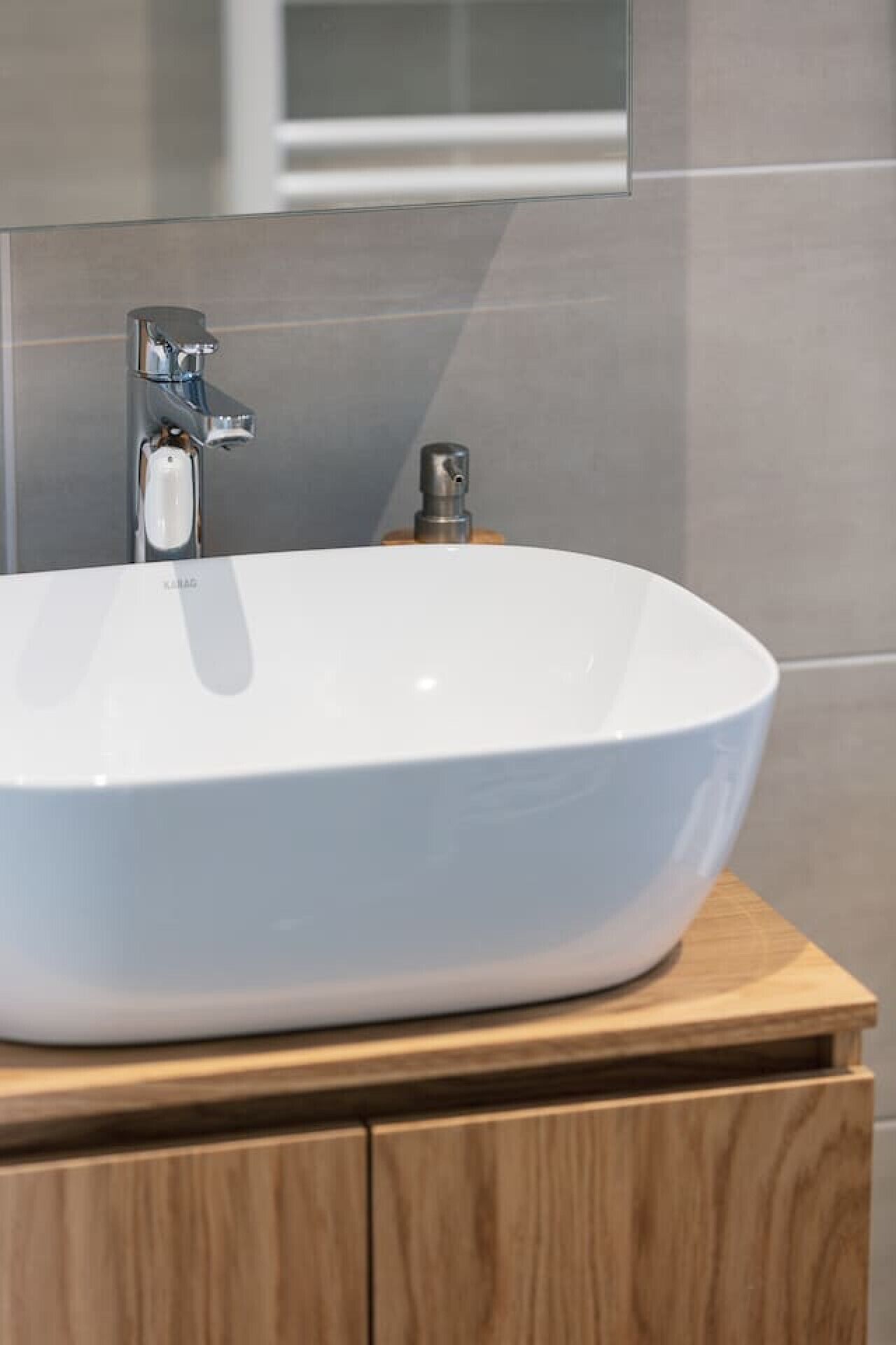 A white oval sink on a wooden vanity with a chrome faucet.