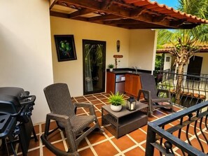 A patio with two wicker chairs, a small table with a plant, and a grill.