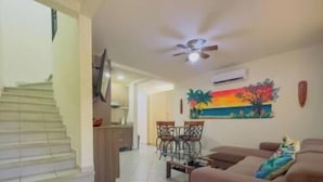 A living room with a sofa, a coffee table, and a dining area with chairs and a table. - Jade A13 - Tropical Two-Story Retreat with Pool Views (City Playas del Coco)