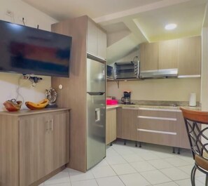A kitchen with a refrigerator, microwave, and a TV mounted on the wall.