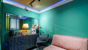 Une pièce aux murs de couleur turquoise, avec un canapé rose, un meuble avec des portes miroir et une petite table sur laquelle se trouvent une lampe et des objets décoratifs.