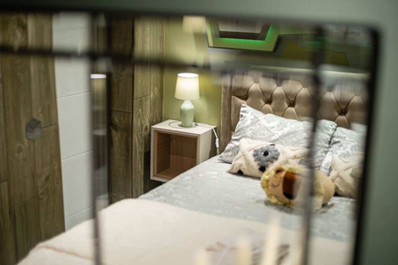 A bedroom with a bed, a nightstand, a lamp, and a teddy bear.