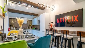 Une cuisine moderne avec un coin repas, un bar doté de tabourets et un grand téléviseur affichant le logo de Netflix.