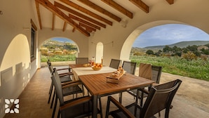 A dining area with a wooden table and chairs, a view of a vineyard, and a rustic interior with exposed wooden beams.