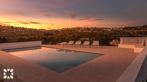 A rooftop infinity pool with lounge chairs and a view of a hilly landscape during sunset.