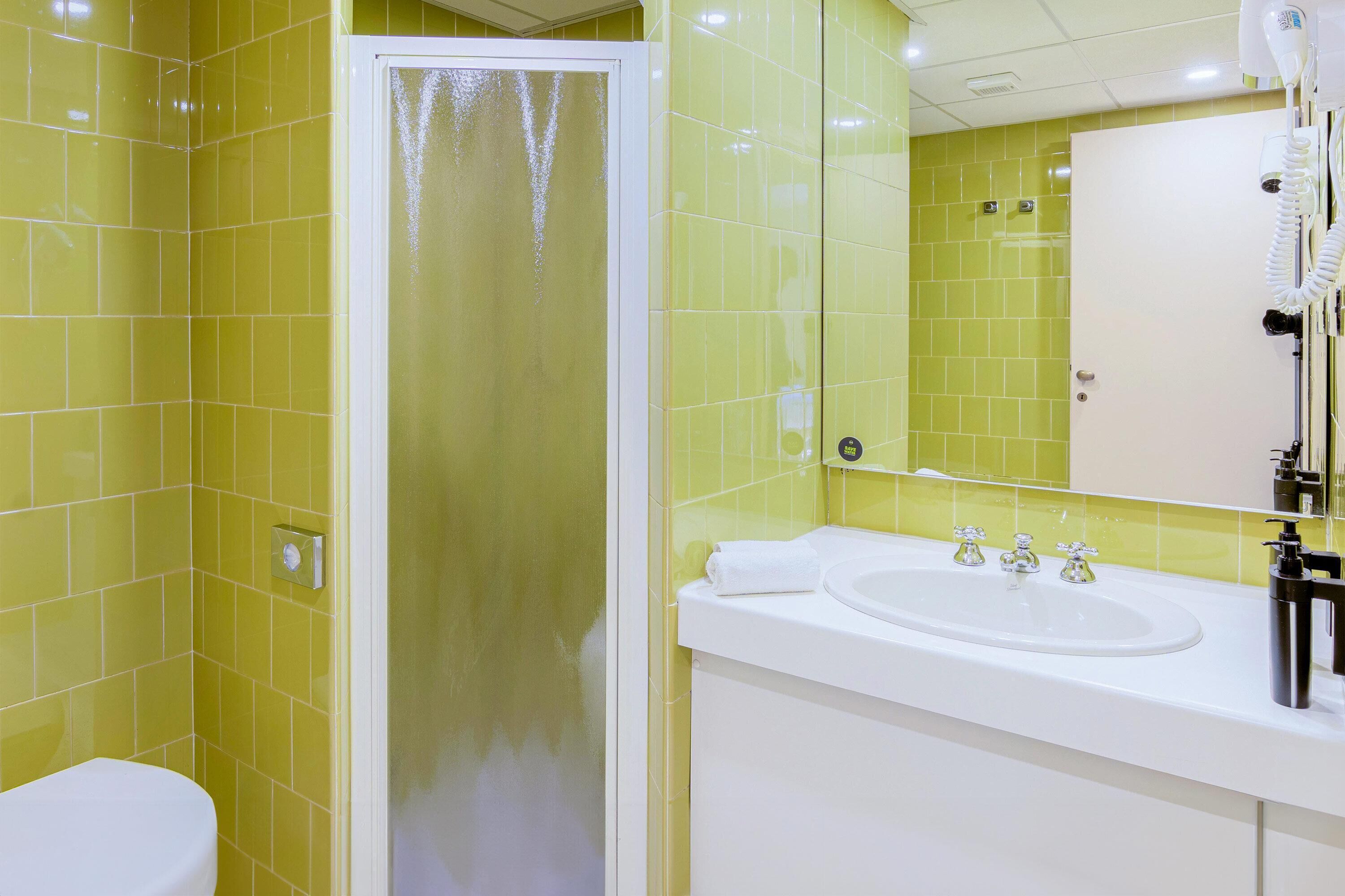 Ein Badezimmer mit gelben Fliesen, einem weißen Waschbecken und einem Spiegel.