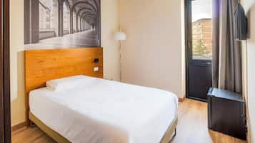 Et hotelværelse med en seng med trægavle, et fladskærms-tv, et billede af en arkitektonisk korridor og udsigt til bygninger gennem vinduet.