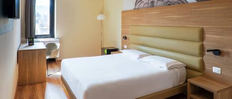 Una habitación de hotel con una cama grande, un escritorio, una silla, un televisor y una ventana con cortinas.