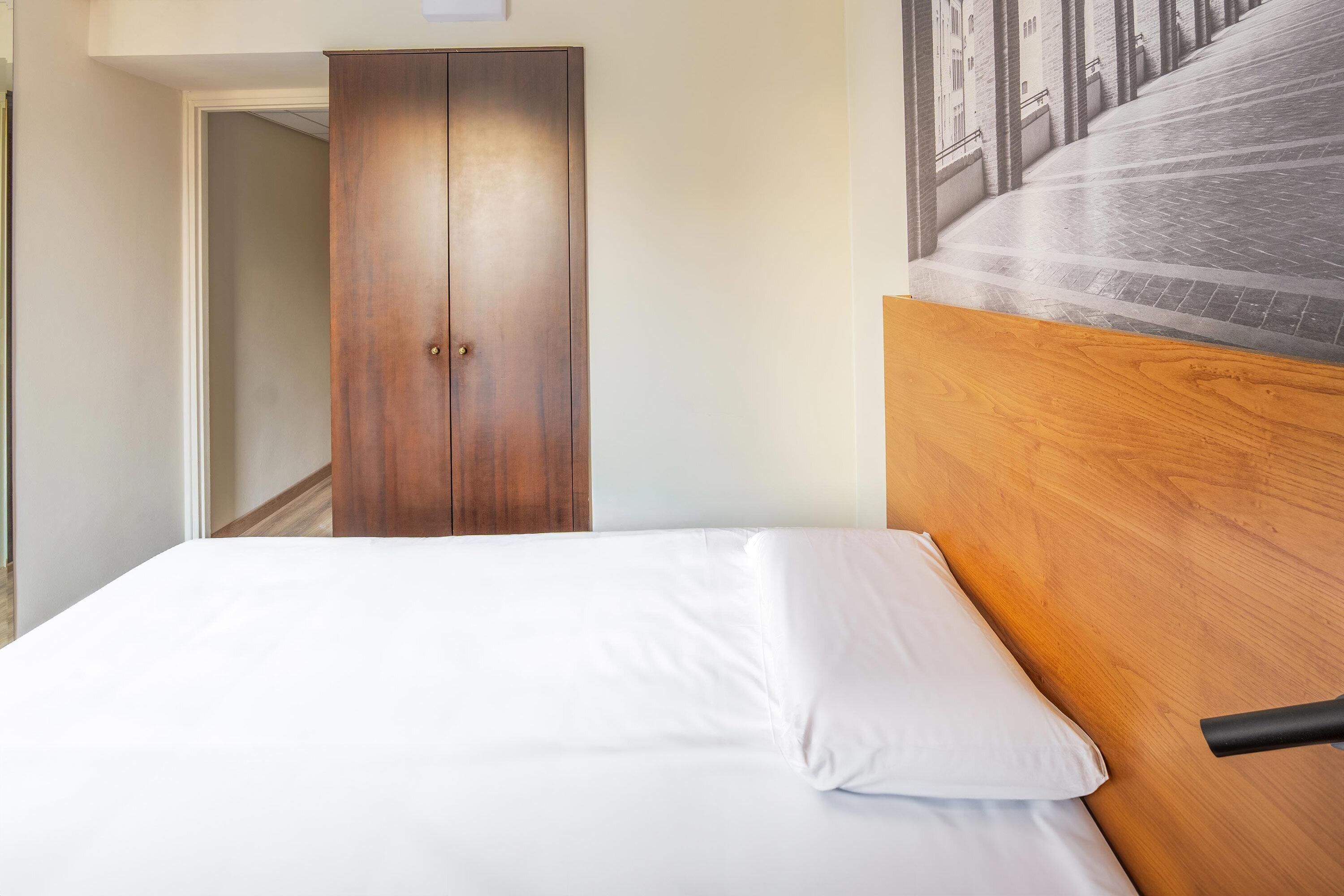 A hotel room with a wooden headboard, a white bed, and a wardrobe.