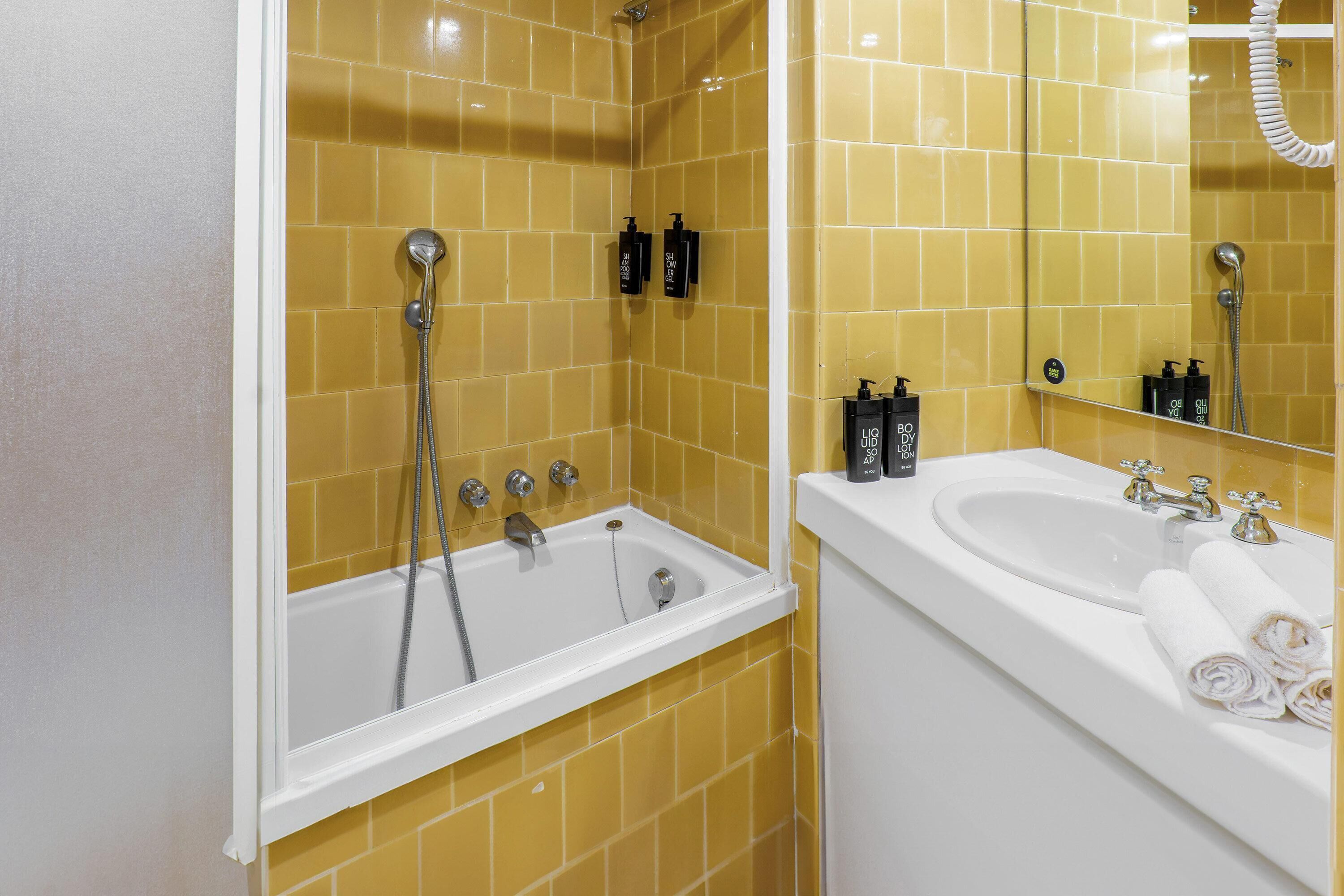 Une salle de bain avec des murs recouverts de carreaux jaunes, une baignoire blanche et un lavabo avec un miroir.
