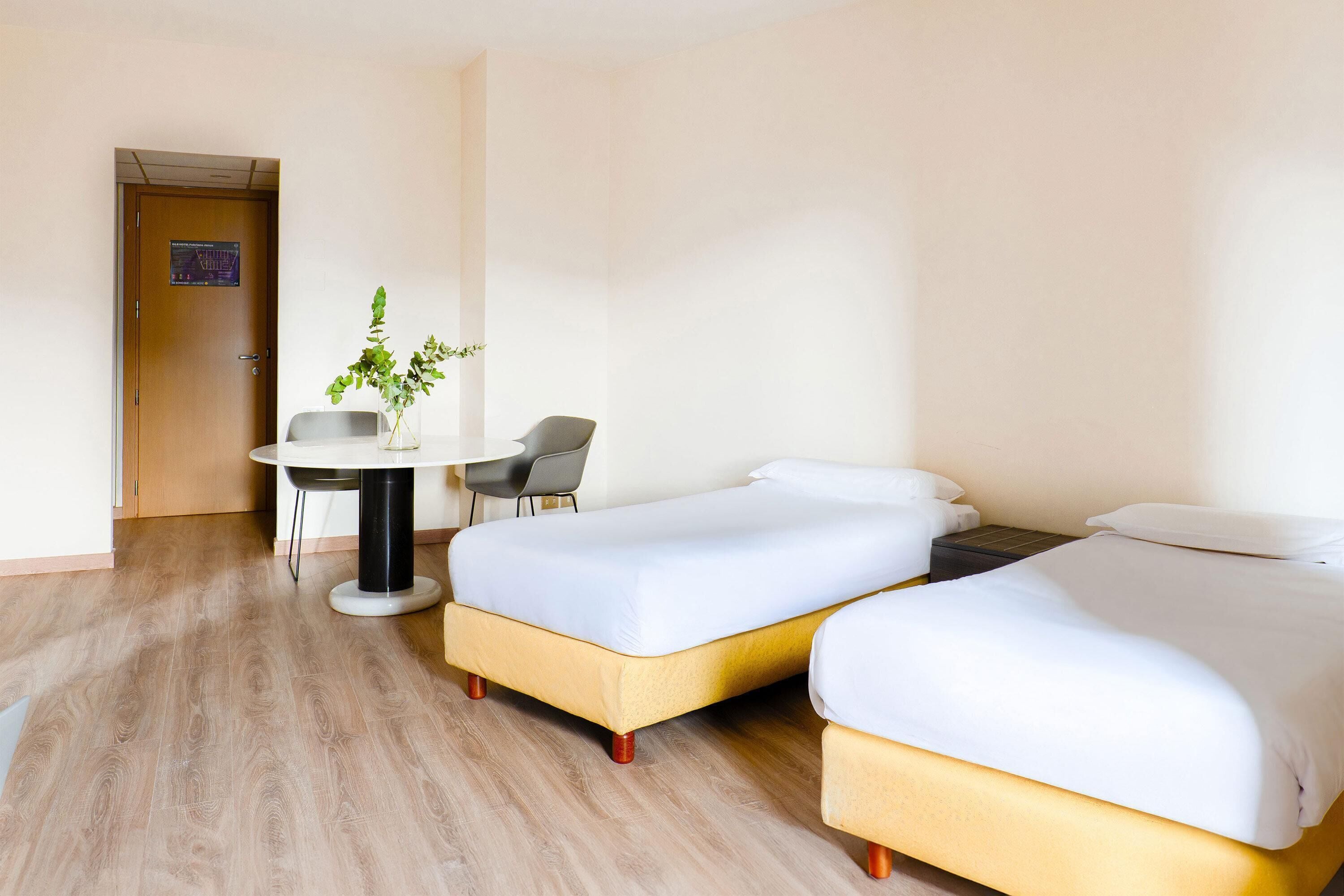 Ein Hotelzimmer mit zwei Betten, einem kleinen Tisch mit Stuhl und einer Zimmerpflanze.