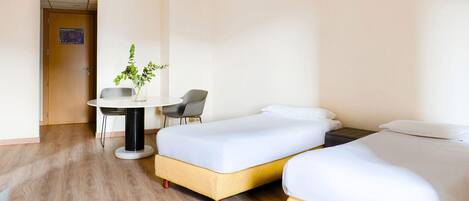 Una habitación de hotel con dos camas, una mesita pequeña con una silla y una planta en maceta.