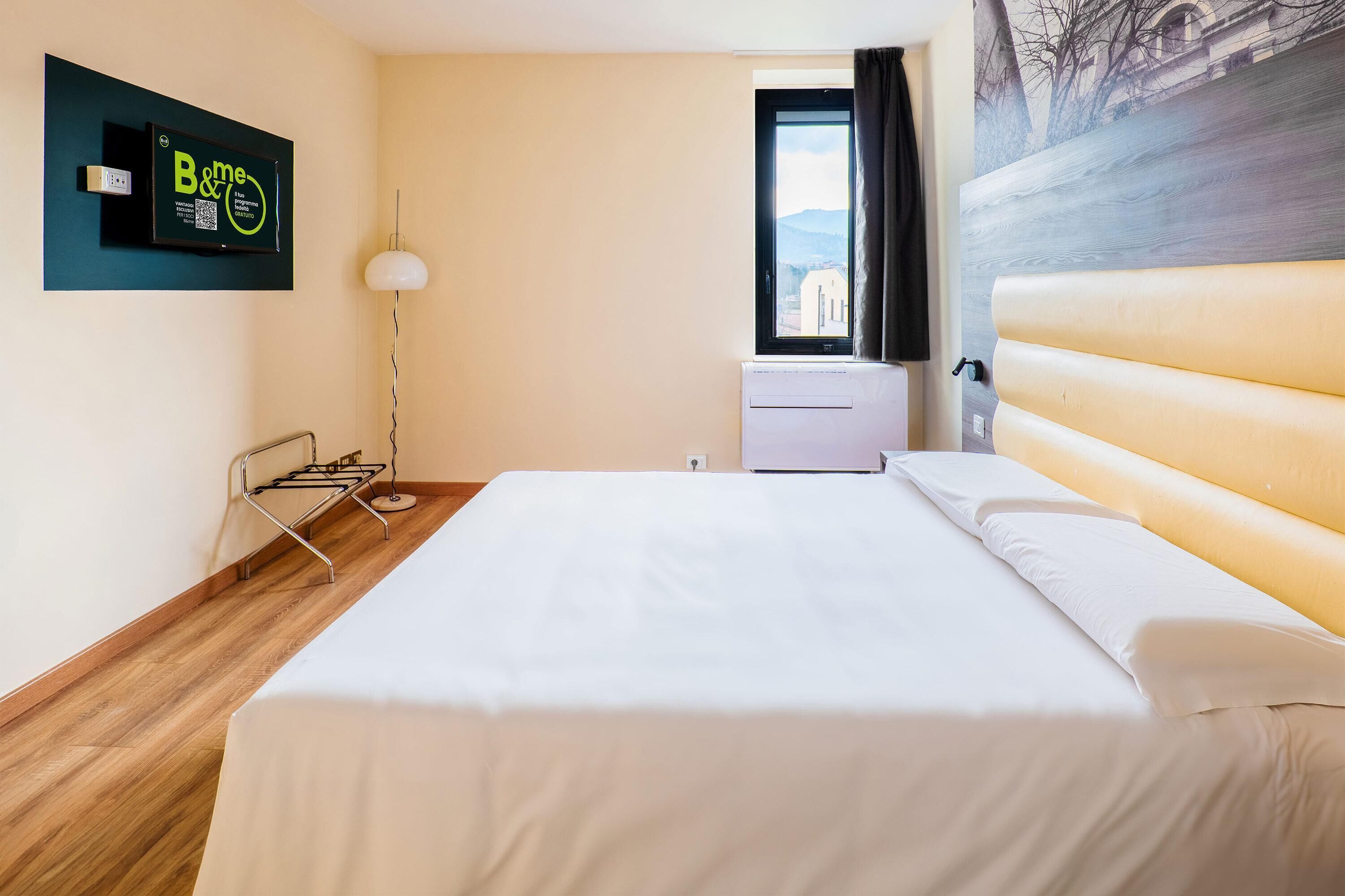 Habitació d'hotel amb llit, televisió penjada a la paret, finestra amb vistes i aire condicionat fixat a la paret.