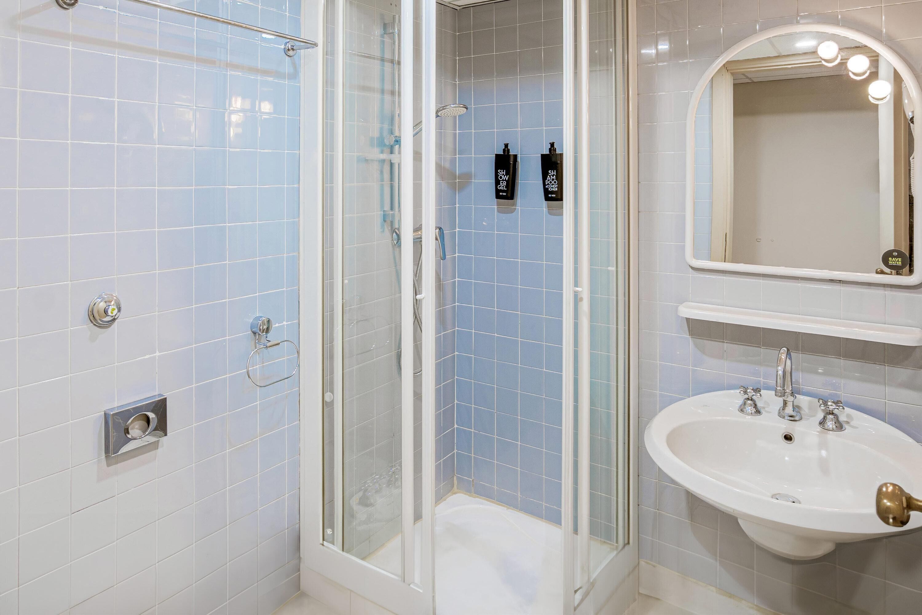 Un baño con ducha acristalada, un lavabo blanco con grifo dorado y un espejo con iluminación.