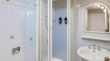 Un baño con ducha acristalada, un lavabo blanco con grifo dorado y un espejo con iluminación.