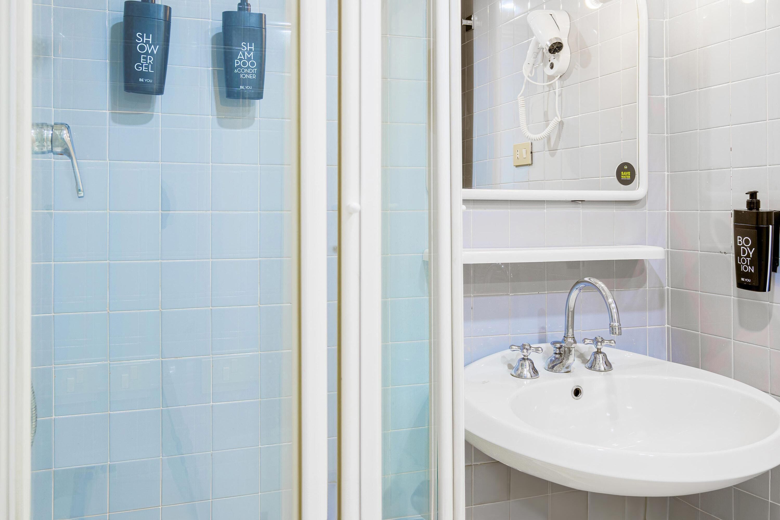 A bathroom with a shower, a sink, and two bottles of shower gel on the wall.