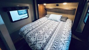 A bedroom with a bed, a mounted TV, and a headboard with built-in lighting. - Secluded Lakeside RV Experience (Bridgeport)