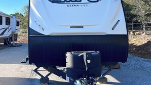 A white MPG ULTRA-LITE RV with a black lower section, a hitch, and a chain. - Secluded Lakeside RV Experience (Bridgeport)
