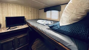 A compact RV bedroom with a bed, a small TV, and a wooden cabinet. - Secluded Lakeside RV Experience (Bridgeport)