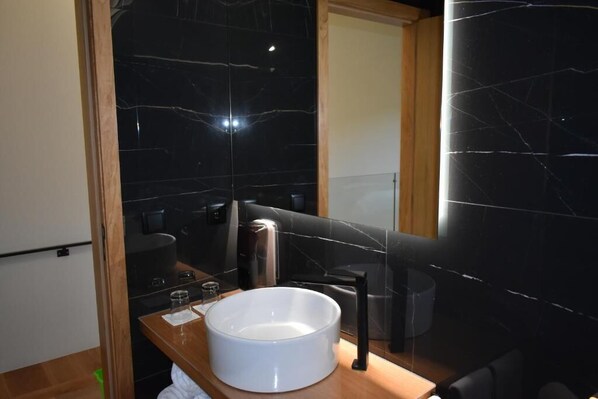 A modern bathroom with a large white sink, black marble walls, and a wooden vanity. - Empreendimento Serra (Covilhã)