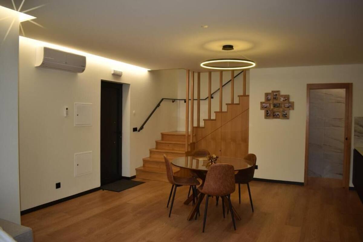 Ein modernes Wohnzimmer mit einer Holztreppe, einem Essbereich mit rundem Tisch und Stühlen sowie einer Wand-Klimaanlage.
