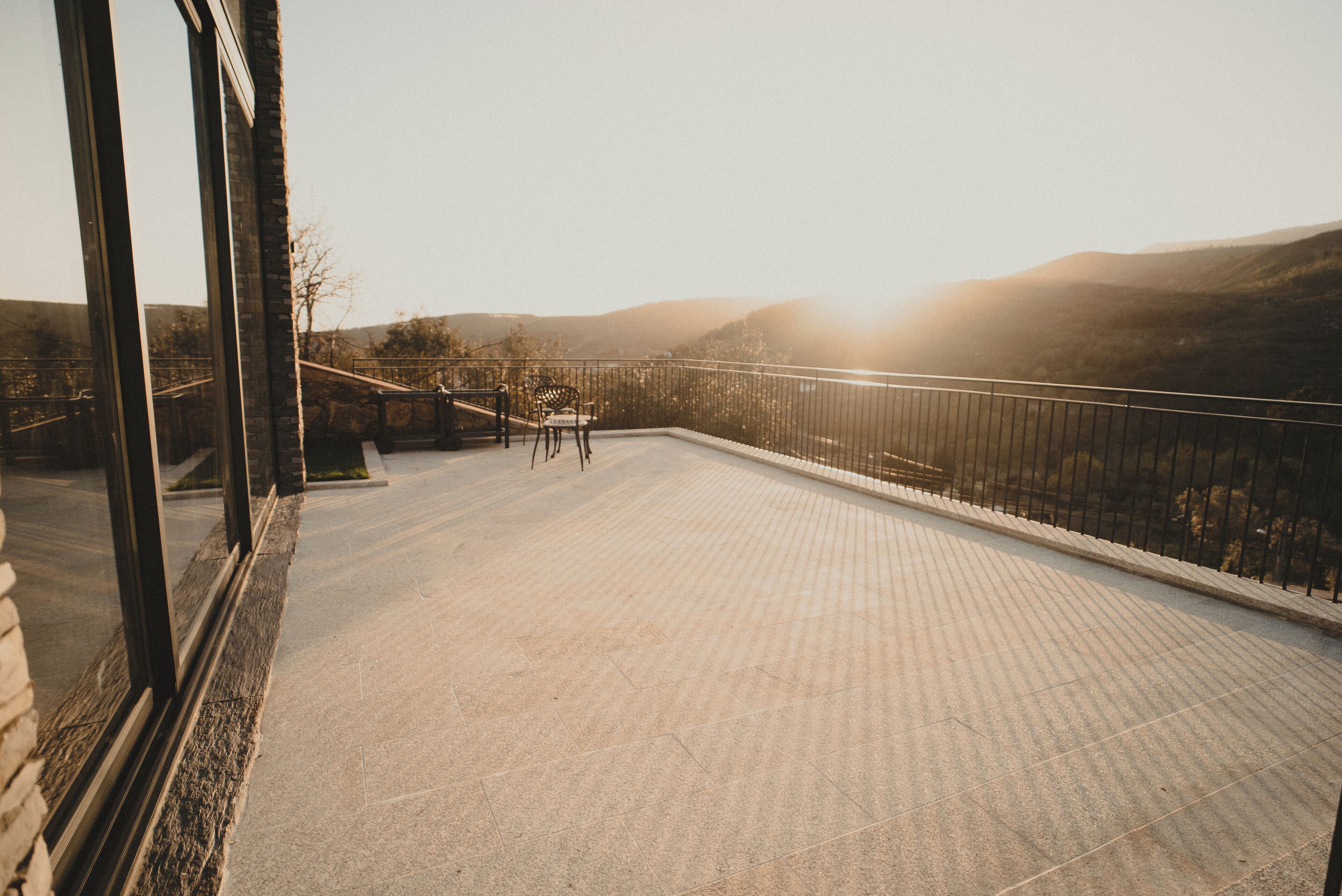 A balcony with a view of hills, a table, and chairs.