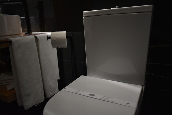 Des toilettes blanches avec une étiquette bien visible et un rouleau de papier toilette accroché au mur.