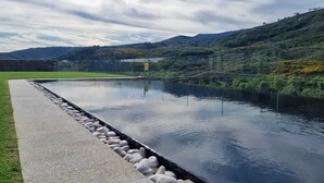 A serene outdoor pool with a stone border, surrounded by lush greenery and hills. - Empreendimento Serra (Covilhã)