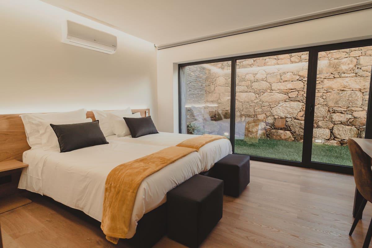 Ein modernes Schlafzimmer mit einem großen Bett, einer durch das Fenster sichtbaren Steinwand und einem Holzboden.