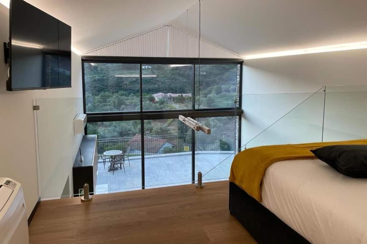 Ein modernes Schlafzimmer mit großem Fenster, einem Bett, einem Schreibtisch und einem an der Wand befestigten Fernseher.